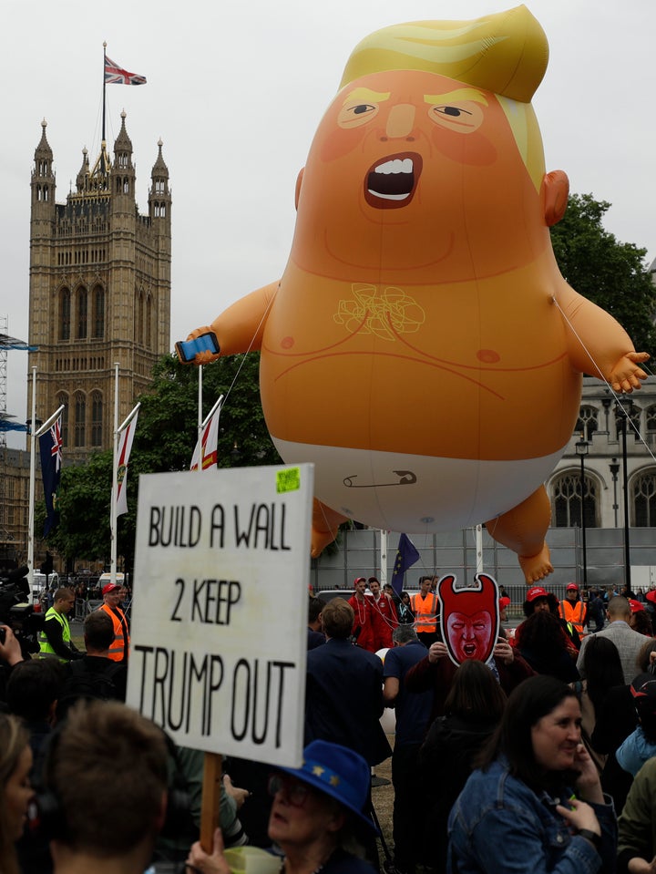 In this June 4, 2019 file photo, a woman holds up a banner standing next to the "Trump Baby" blimp as people gather to demonstrate against the state visit of President Donald Trump in Parliament Square, central London.