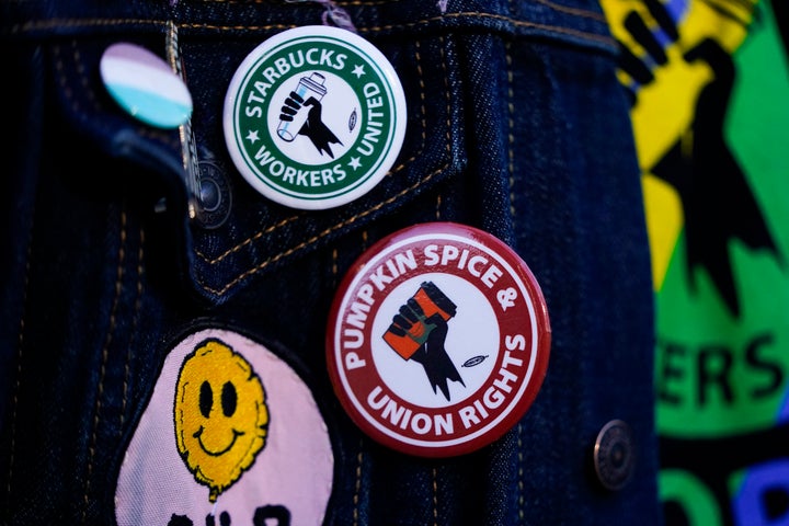 Un empleado usa alfileres sindicales en su chaqueta mientras los trabajadores de Starbucks participan en una huelga y huelga durante el Día de la Copa Roja de la compañía en noviembre de 2023, en el primer tosterio de reserva de la compañía en Seattle. Una coalición de grupos progresivos espera presionar a Starbucks para llegar a un acuerdo con su sindicato de baristas ahora que las negociaciones contractuales se han estancado.