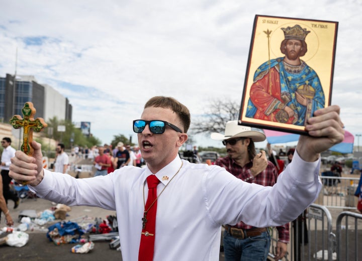 A man carries a cross and an icon near protesters outside the memorial for Charlie Kirk at State Farm Stadium in Glendale, Arizona, on September 21, 2025. (Photo by ANDREW CABALLERO-REYNOLDS / AFP) (Photo by ANDREW CABALLERO-REYNOLDS/AFP via Getty Images) 