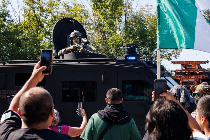 An ICE officer watches protestors as a Lenco BearCat vehicle drives to the scene in the Brighton Park neighborhood of Chicago, on Saturday, Oct. 4, 2025, after protesters learned that U.S. Border Patrol shot a woman Saturday morning on Chicago's Southwest Side. (Anthony Vazquez/Chicago Sun-Times via AP)