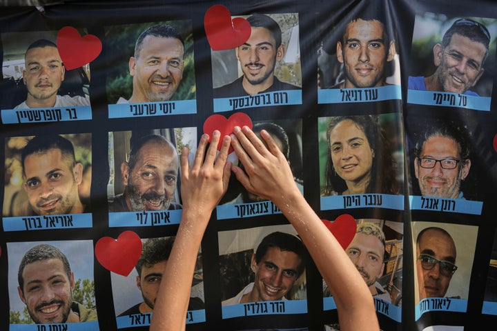 Hands paste a heart-shaped sticker onto a banner with pictures of Israeli hostages during a a gathering at a plaza known as hostages square in Tel Aviv, Israel, on Oct. 13, 2025.