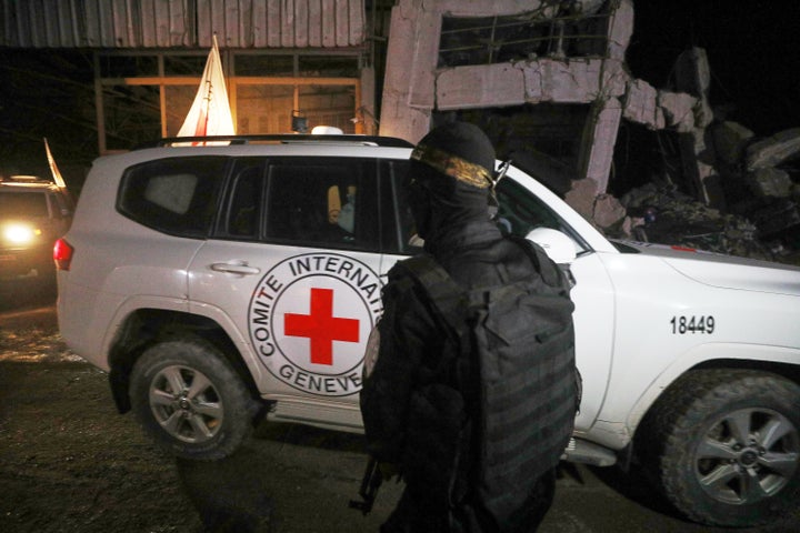 A gunman wearing the uniform of the al-Qassam Brigades, the military wing of Hamas, stands guard as Red Cross vehicles allegedly transporting coffins containing the bodies of four deceased hostages leave a warehouse for Israel, in Gaza City, on Oct. 14, 2025.