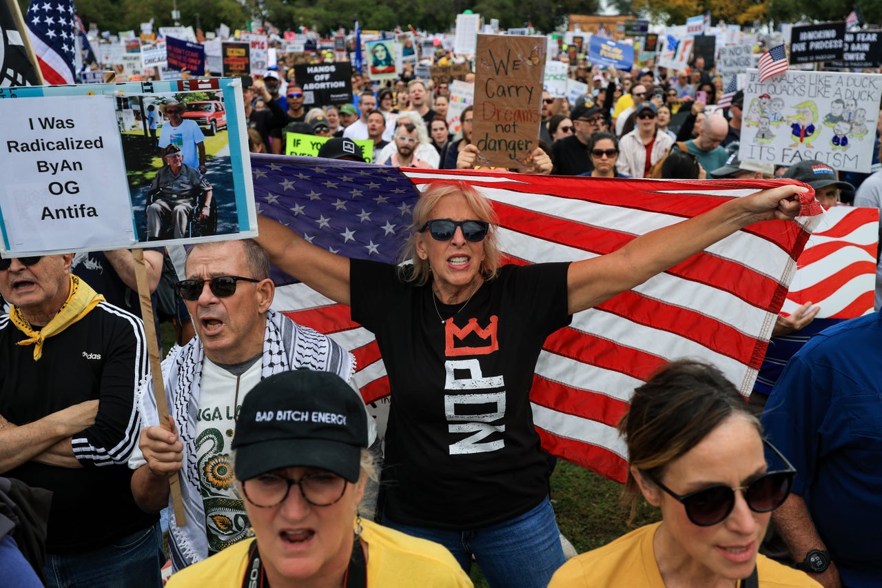 A demonstrator holds up an American flag during a "No Kings" protest in Chicago, Illinois. Another holds a sign reading "I Was Radicalized By An OG Antifa," featuring what appears to be a photo of a veteran.