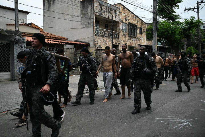 Police officers escort alleged criminal arrested during the Operacao Contencao (Operation Containment) at the Vila Cruzeiro favela, in the Penha complex, in Rio de Janeiro, Brazil, on October 28, 2025. At least 2,500 security forces agents took part in an operation to arrest drug traffickers from the Comando Vermelho (CV), which resulted in 64 people dead, authorities reported. (Photo by Mauro PIMENTEL / AFP) (Photo by MAURO PIMENTEL/AFP via Getty Images) 