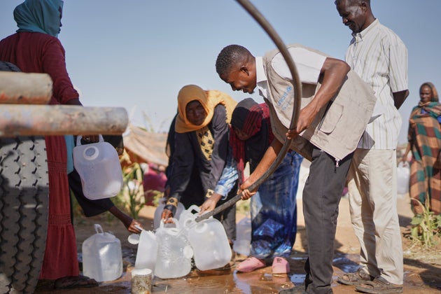 スーダン国軍（SAF）と即応支援部隊（RSF）の戦闘から逃れ、タウィラの避難民キャンプで、水をトラックから汲むエル・ファーシルの避難民の子どもたちと家族（2025年10月27日）