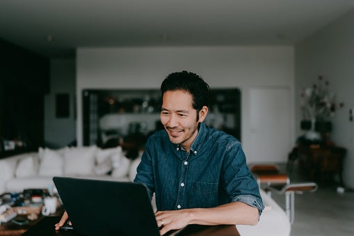A smiling man works at home on a laptop.