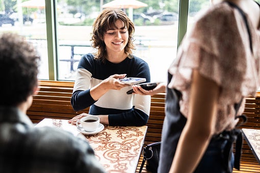 Young woman pays her bill with a smartphone in a coffee shop.