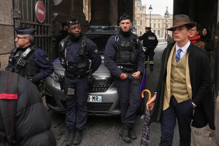 Pedro Elias Garzon Delvaux, right, walks past as police officers block an entrance to the Louvre after thieves carried out a daylight raid on the French crown jewels.