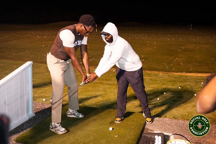 An experienced golfer helps an attendee with his swing.