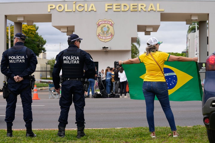 A supporter of Brazil's former President Jair Bolsonaro holds a Brazilian flag outside the Federal Police headquarters, where Bolsonaro is under arrest in Brasilia, Brazil, Saturday, Nov. 22, 2025, after Brazil's Federal Police arrested Bolsonaro preemptively on Saturday, days before he was due to start serving his 27-year-plus prison sentence for leading a coup attempt. (AP Photo/Eraldo Peres)