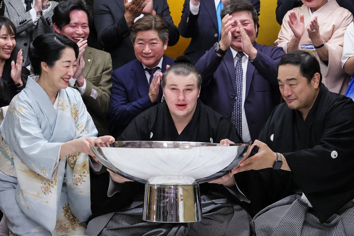 Aonishiki poses with a large cup to celebrate after winning the Grand Sumo Tournament.