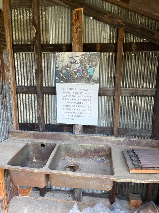 ウトロ平和祈念館で野外展示されている、放火によって黒く焼け焦げた住居を写した写真と、燃え残った流し台
