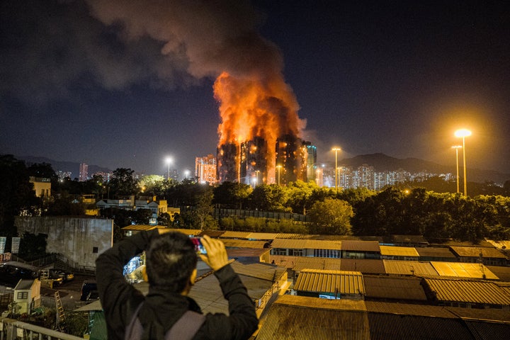 Dying Toll In Hong Kong Excessive-Rise Fireplace Rises To 36, With 279 Nonetheless Lacking 2 An onlooker takes photos as a major fire engulfs several apartment blocks at the Wang Fuk Court residential estate (background) in Hong Kong's Tai Po district on November 26, 2025. (Photo by AFP via Getty Images)