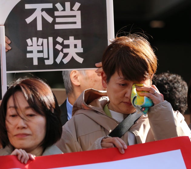 「不当判決」と書かれた旗を持って涙をぬぐう原告の藤井美由紀さん（右）。左は福田理恵さん