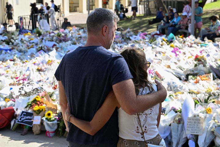 Bondi Seaside Capturing Suspect Charged With Homicide, Terrorism 1 SYDNEY, AUSTRALIA - DECEMBER 17: A couple embrace at the flower memorial beside Bondi Pavilion on December 17, 2025 in Sydney, Australia. (Photo by James D. Morgan/Getty Images)