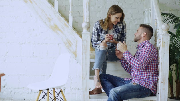 Couple drinking coffee, sitting on stairs at home.