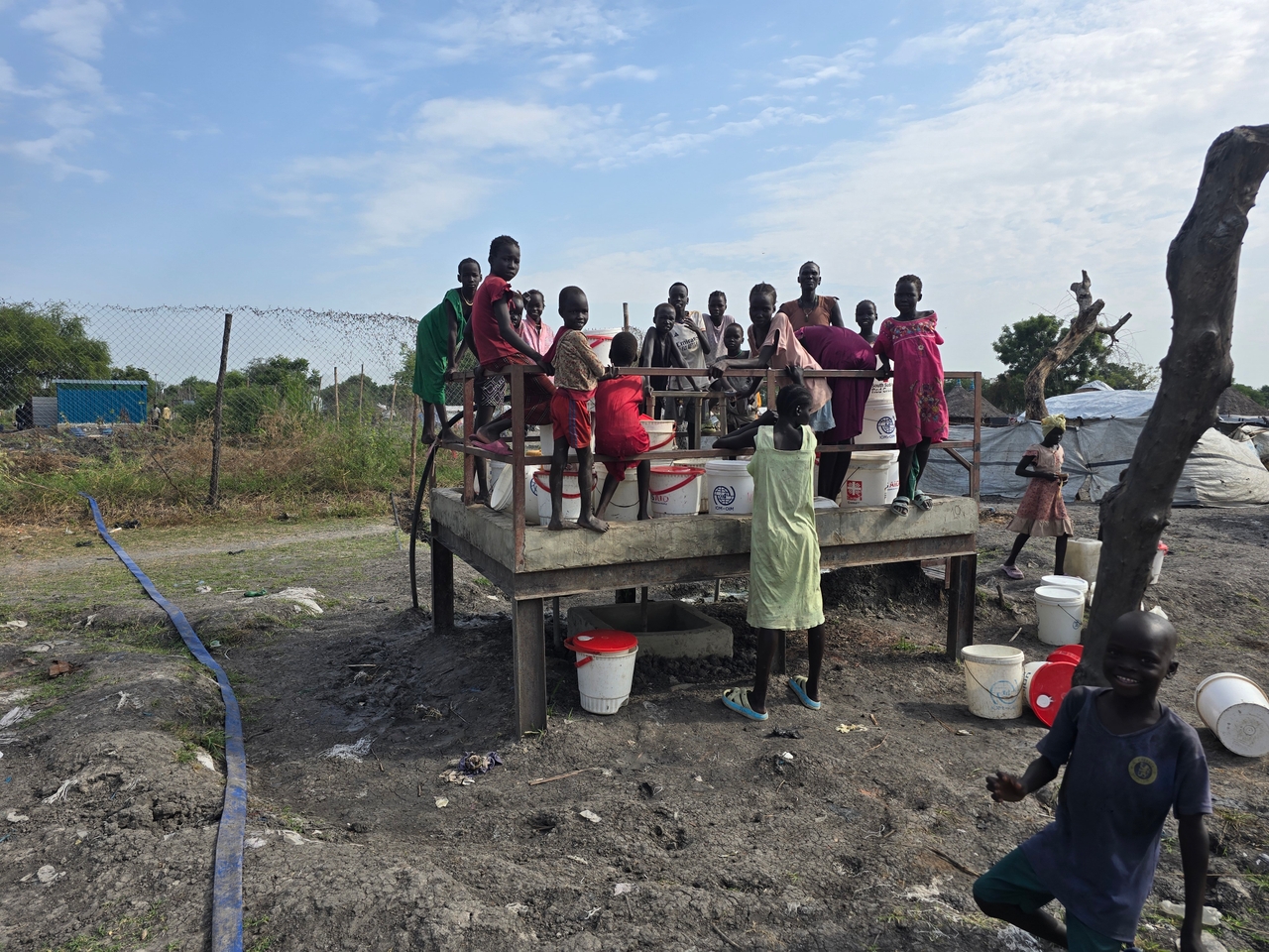 Trump made a perfect storm even more deadly and the 2 Children gather around a water stand opened by the Alaska Health Project in South Sudan.