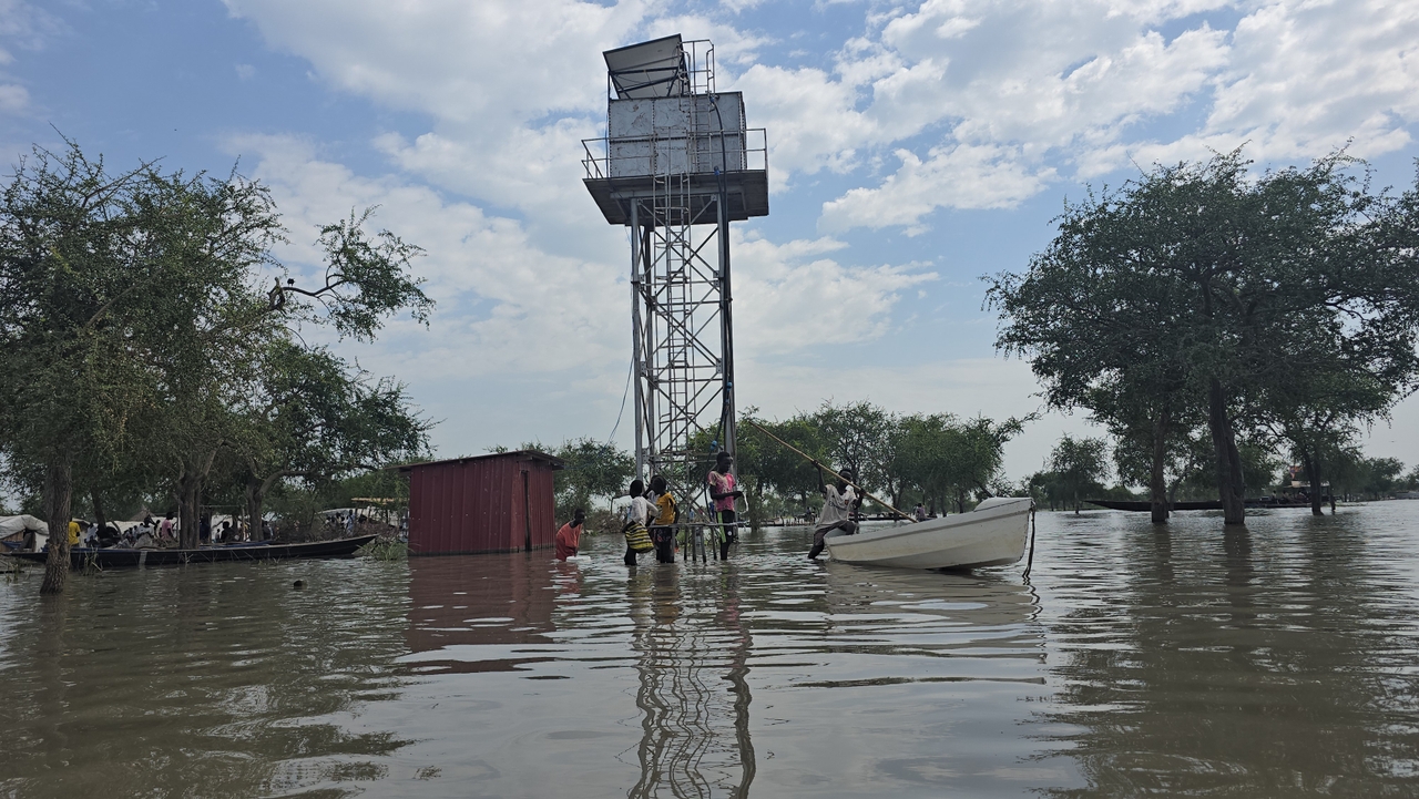 In a Kuernyang, a water tower delivering clean water to a tap stand below. People must access it by boat if they're not tall enough to walk through high flood waters and swampy marshes. The area is flooded by rainwater, and it is next to the airstrip which is also flooded.