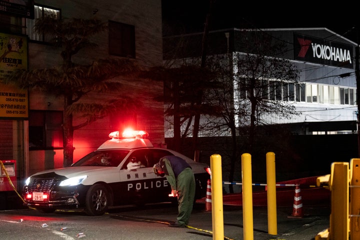 TOPSHOT - A worker bows as a police car leaves the Yokohama Rubber Mishima Plant in Mishima, Shizuoka Prefecture, on December 26, 2025. Fifteen people were injured in a stabbing attack in a rubber factory in central Japan on December 26, during which an unspecified liquid was also sprayed, emergency officials said. (Photo by Yuichi YAMAZAKI / AFP via Getty Images)
