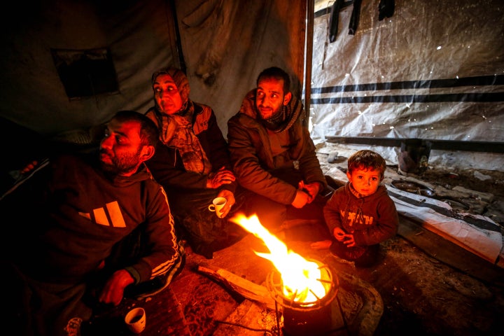 JABALIA, GAZA - DECEMBER 28: A family is seen sitting by the fire as many displaced Palestinians living in the Jabalia area in northern Gaza struggle to carry on their daily lives under harsh conditions amid the rubble left by Israeli attacks on December 28, 2025. Lacking basic necessities, families try to survive in makeshift tents set up near their destroyed homes while coping with cold weather conditions. (Photo by Saeed M. M. T. Jaras/Anadolu via Getty Images)