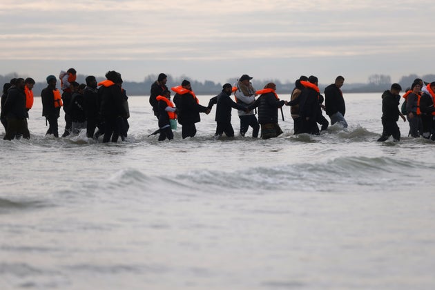 Migrants walk in the water to board a small boat in an attempt to reach Britain, Thursday, Nov. 6, 2025 in Gravelines, northern France. 