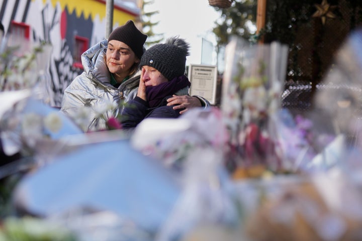 People mourn behind flowers and letters near the sealed off Le Constellation bar, where a devastating fire left dead and injured during the New Year's celebrations in Crans-Montana, Swiss Alps, Switzerland, Friday, Jan. 2, 2026.