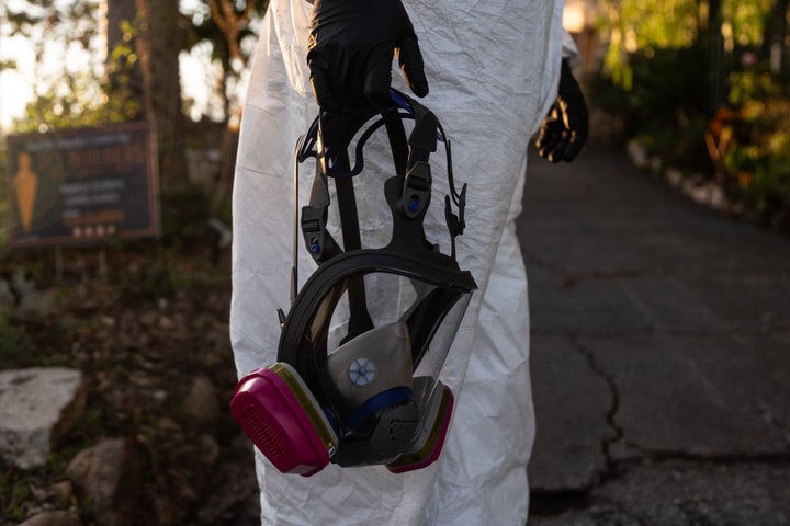 A worker carries a respirator while removing fire debris at a home that survived the Eaton Fire in Altadena, Calif. 