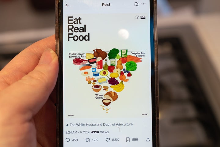 A person holds an iPhone displaying a social media post from the U.S. Department of Health and Human Services showing the Trump administration's revised food pyramid.