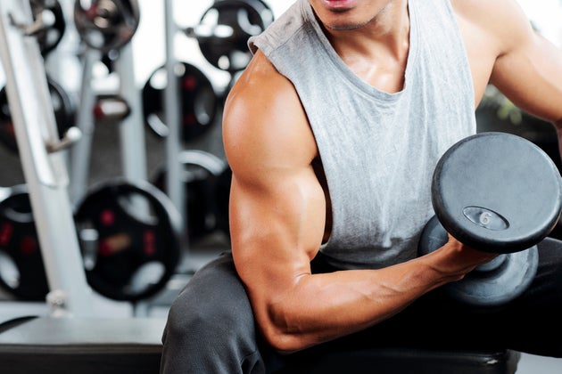 Fit strong man doing biceps curl in gym