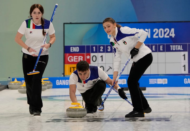Italy's Andrea Gilli, center, throws a stone as teammates Giorgia Maurino and Rebecca Mariani, left, prepare to sweep the ice at the 2024 Winter Youth Olympic Games in Gangneung, South Korea.