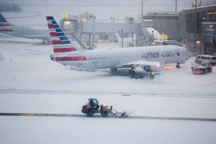 A snow removal machine is seen working while a Boeing 737 American Airlines passenger aircraft is parked at gate on the tarmac of LaGuardia airport in New York on January 25, 2026. A massive winter storm on January 24, 2026 dumped snow and freezing rain on New Mexico and Texas as it swept across the United States towards the northeast, threatening tens of millions of Americans with blackouts, transportation chaos and bone-chilling cold. Shoppers stripped supermarket shelves as the National Weather Service (NWS) forecast huge snowfall in some areas and possibly "catastrophic" ice accumulations. (Photo by CHARLY TRIBALLEAU / AFP via Getty Images)