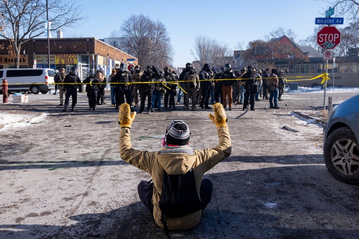A protester sits on the street with his arms up in front of a gaggle of federal agents and Minneapolis Police on W. 27th St and Nicollet Avenue in south Minneapolis after Alex Pretti was fatally shot by federal agents in the area early Saturday morning, January 24, 2026.