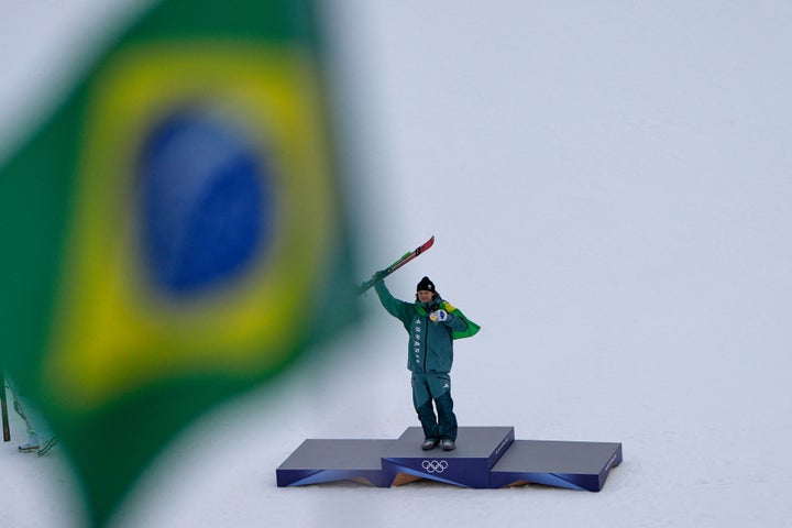Brazilian Lucas Pinheiro Braathen, winner of a men's alpine ski and giant slalom race, poses on the podium framed by a Brazilian flag during the 2026 Winter Olympics in Bormio, Italy, Saturday, Feb. 14, 2026. (AP Photo/John Locher)