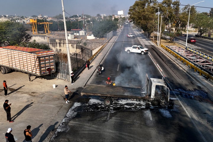 A man extinguishes a burning truck set on fire by organised crime groups in response to an operation in Jalisco to arrest a high-priority security target, at one of the main avenues in Zapopan, state of Jalisco, Mexico, on February 22, 2026. Armed civilians blocked several roads in the state of Jalisco, in western Mexico, following an operation by federal forces in the town of Tapalpa, local authorities reported. Jalisco, which will host four matches of the upcoming 2026 World Cup, is home to the powerful Jalisco New Generation Cartel (CJNG), and has been rocked by several episodes of violence in recent years. (Photo by Ulises RUIZ / AFP via Getty Images)