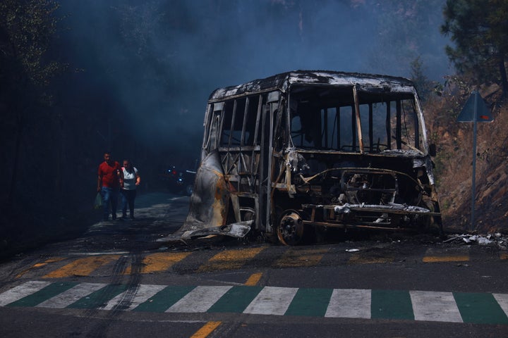 Pedestrians walk past a charred vehicle after it was set on fire, on a road in Cointzio, Michoacán state, Mexico, on Feb. 22, 2026, after the death of the leader of the Jalisco New Generation Cartel, Nemesio Rubén Oseguera Cervantes, known as "El Mencho."