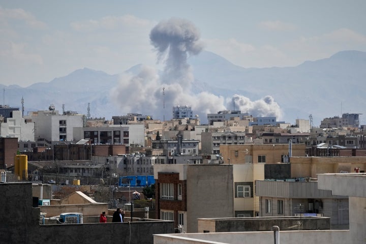 People watches from a rooftop as a plume of smoke rises after a strike in Tehran, Iran, Sunday, March 1, 2026. (AP Photo/Vahid Salemi)