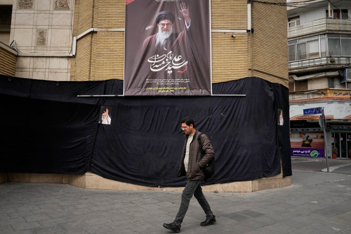 A man walks by a picture of the late Iranian Supreme Leader Ayatollah Ali Khamenei hanging on a black sheet along the side of a mosque in Tehran, Iran, on March 2, 2026.