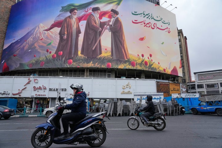 Motorbikes drive past a billboard depicting Iran’s late Supreme Leader Ayatollah Ali Khamenei, center, handing the country’s flag to his son and successor Ayatollah Mojtaba Khamenei, right, as the late revolutionary founder Ayatollah Ruhollah Khomeini stands at left, in a square in downtown Tehran, Iran, Tuesday, March 10, 2026. (AP Photo/Vahid Salemi)