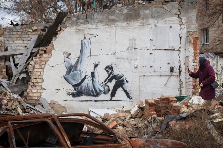 A woman takes a picture of artwork that might have been made by British street artist Banksy on a building destroyed by fighting in Borodyanka, in the Kyiv region, Ukraine, Sunday, Nov. 13, 2022. (AP Photo/Andrew Kravchenko)