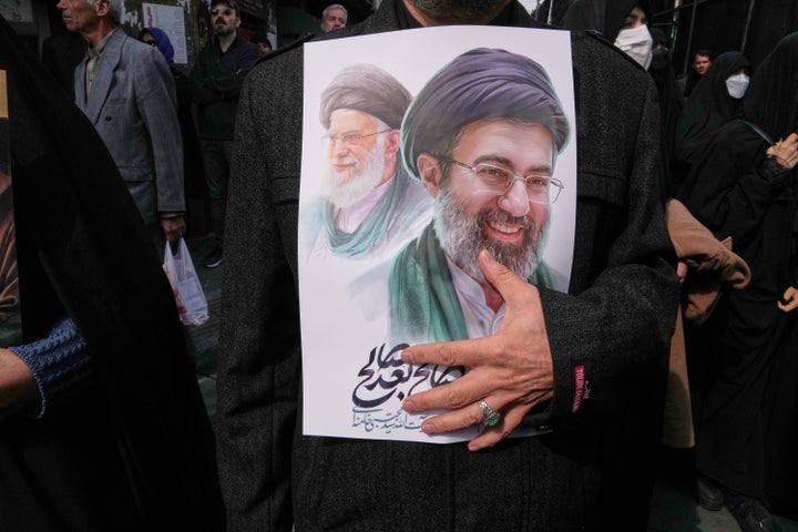 FILE - A mourner holds a poster depicting Ayatollah Mojtaba Khamenei, right, the successor to his late father Ayatollah Ali Khamenei, left, as supreme leader, during the funeral procession for senior Iranian military officials and civilians killed during the U.S.-Israel campaign in Tehran, Iran, March 11, 2026. (AP Photo/Vahid Salemi, File)