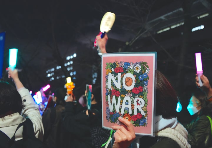 「NO WAR」のプラカードとペンライトを掲げる女性(2026年3月19日撮影)