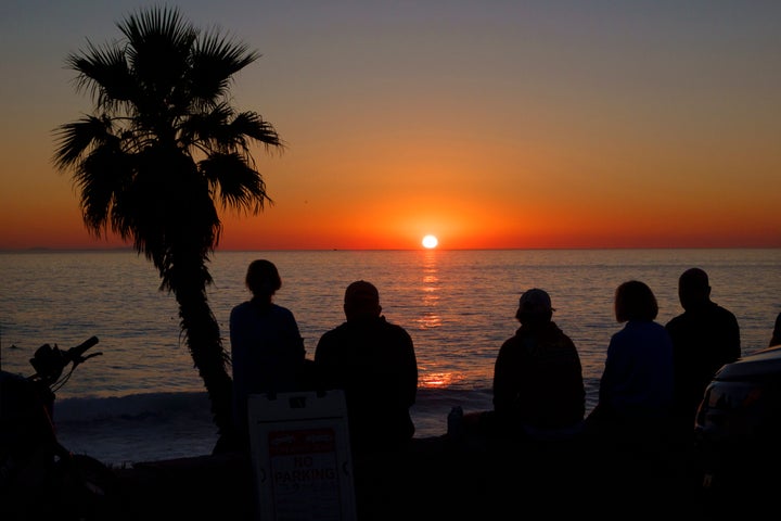 People watch the sun set on the horizon of the Pacific Ocean in La Jolla during a record-setting winter heat wave that has blanketed Southern California on March 19, 2026 in San Diego, CA.
