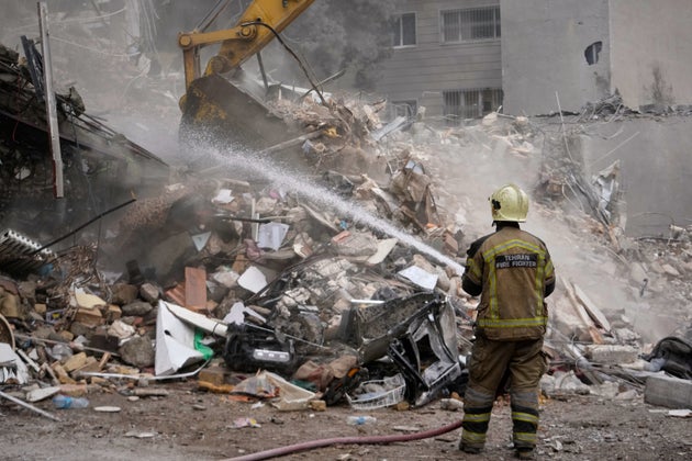 A firefighter hoses down smoldering rubble as a bulldozer clears debris at a residential building hit in an earlier US-Israeli strike in Tehran.