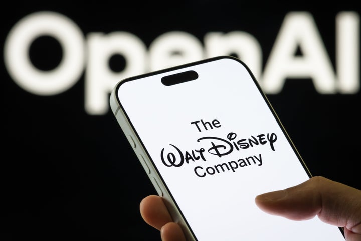 A smartphone displays the logo of The Walt Disney Company with the OpenAI logo visible in the background on Dec. 16, 2025. 
