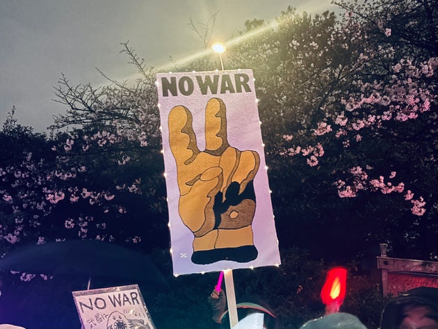咲き始めた桜の木の前で掲げられた「NO WAR」のプラカードとペンライト