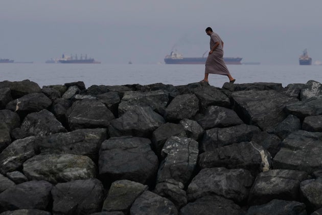 A man walks along the shore as oil tankers and cargo ships line up in the Strait of Hormuz, seen from Khor Fakkan, United Arab Emirates, Wednesday, March 11, 2026.