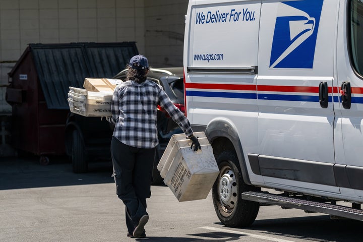 A United States Postal Service (USPS) worker carries containers and packages from a vehicle in Tracy, California, US, on Wednesday, March 25, 2026. 