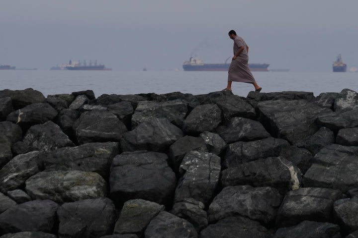FILE- A man walks along the shore as oil tankers and cargo ships line up in the Strait of Hormuz, seen from Khor Fakkan, United Arab Emirates, March 11, 2026.