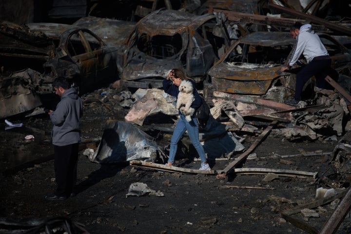 A woman holds her dog as she walks past burned cars a day after an Israeli airstrike in Beirut, Lebanon, Thursday, April 9, 2026. (AP Photo/Emilio Morenatti)