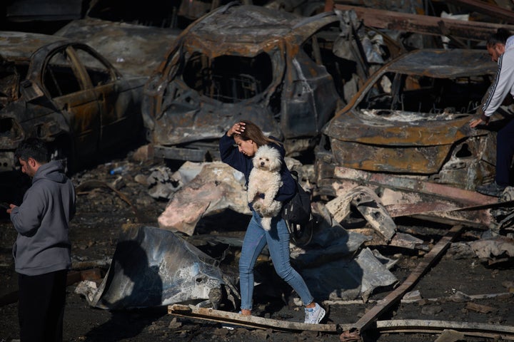 A woman holds her dog as she walks past burned cars a day after an Israeli airstrike in Beirut, Lebanon on Thursday.
